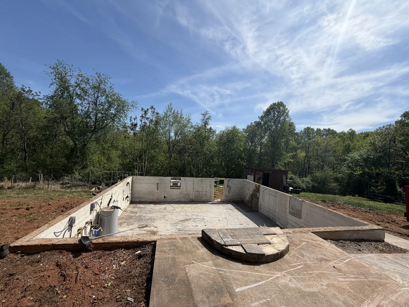 Excavator on cleared lot with poured foundation after house demolition in Goodview